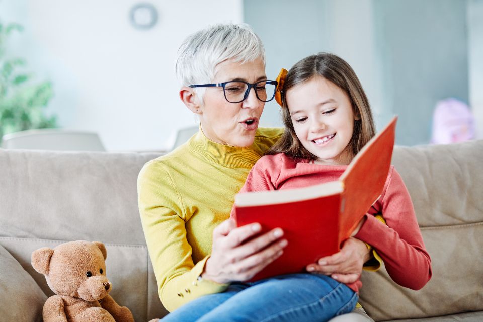 elder adult woman sitting and reading a book with granddaughter